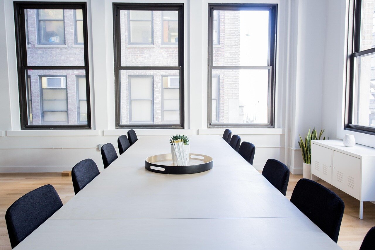 An empty modern conference room with a long table, chairs, and large windows.