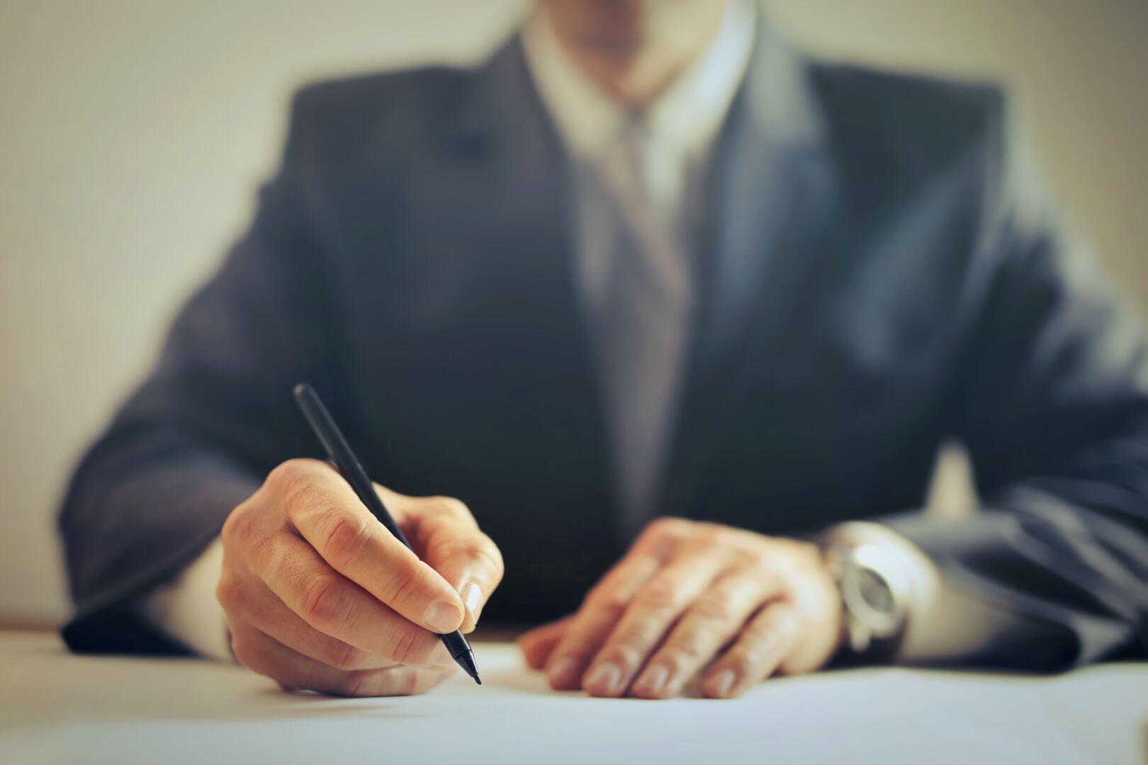 Close-up of a hand signing a document with a pen at a desk.