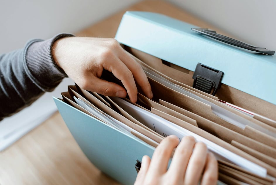Close-up of a person's hands sorting paper files in a portable accordion folder organizer on a wooden desk.
