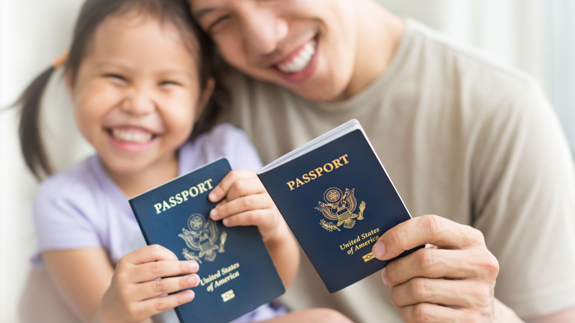 A parent and young child smiling at home while holding two United States passports.