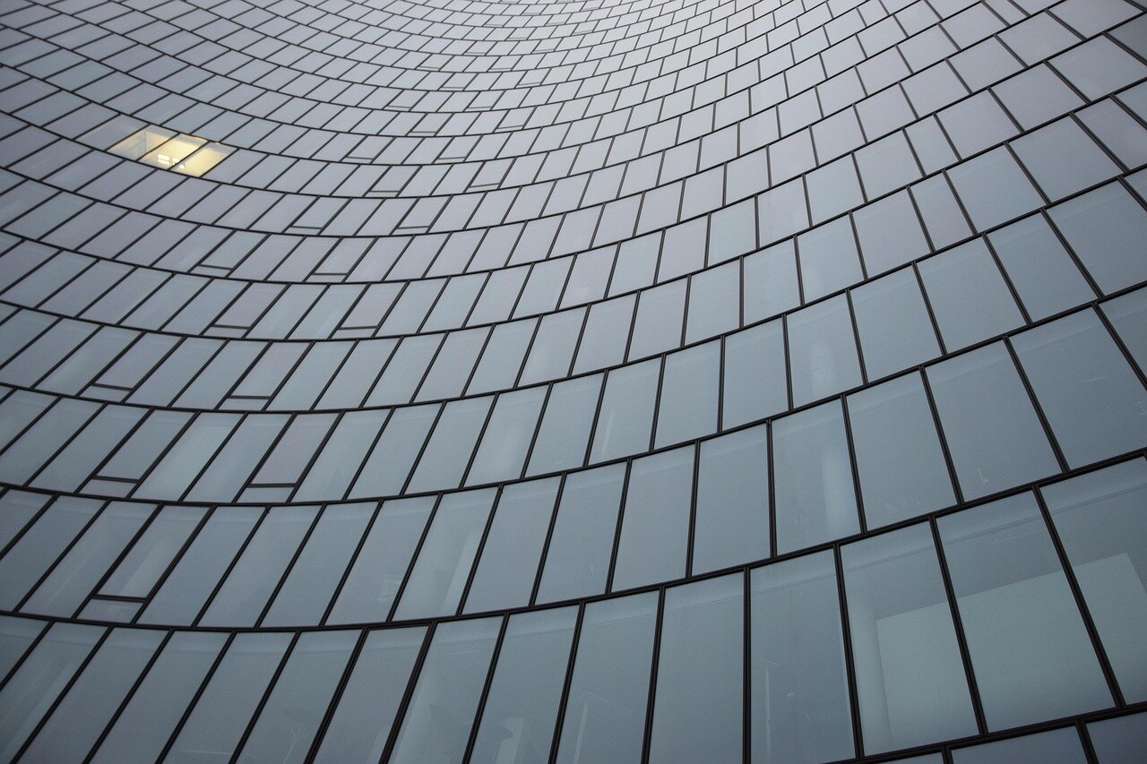 Close-up of a curved glass office building facade against an overcast sky.
