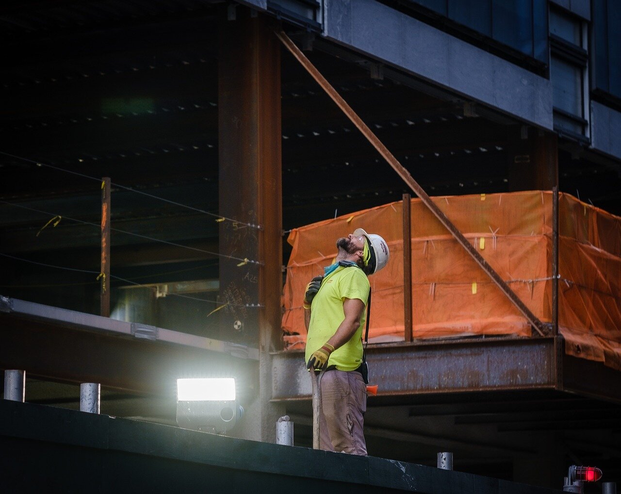 A construction worker in a hard hat and high-visibility shirt standing on a steel-frame building site