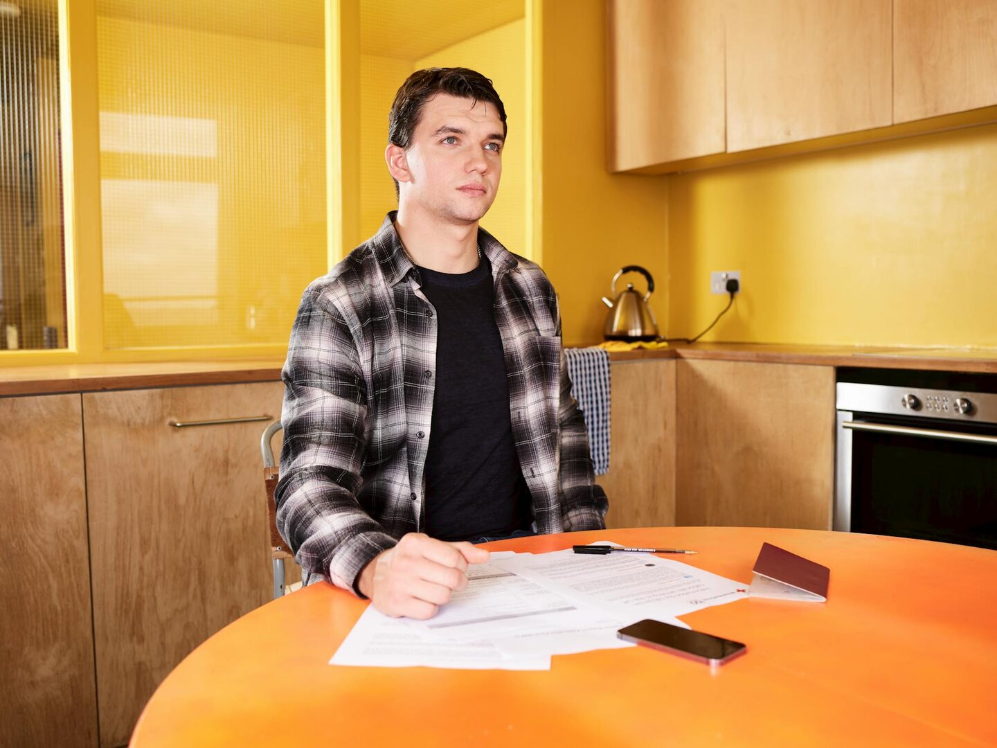 Immigrant worker seated at a kitchen table reviewing pay documents and paperwork, calm and focused.